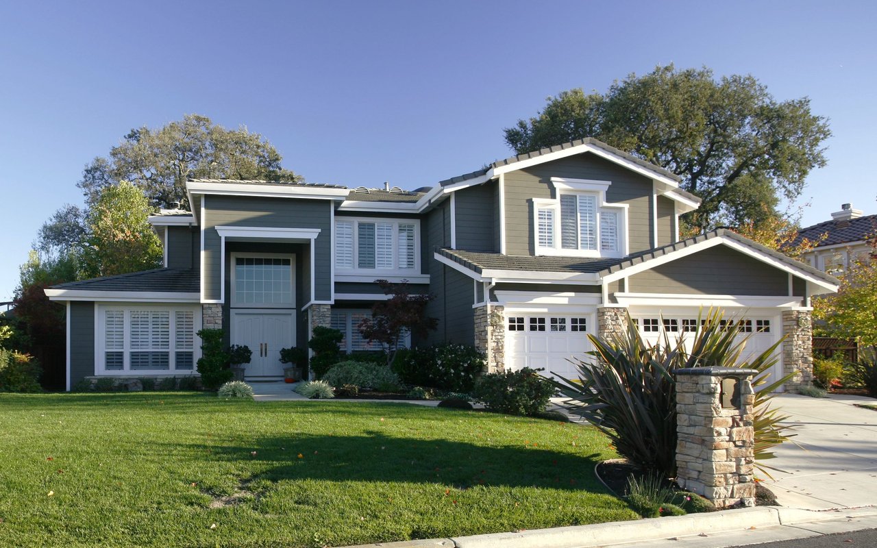 Two-story gray house with white trim, stone accents, and a broad front lawn.