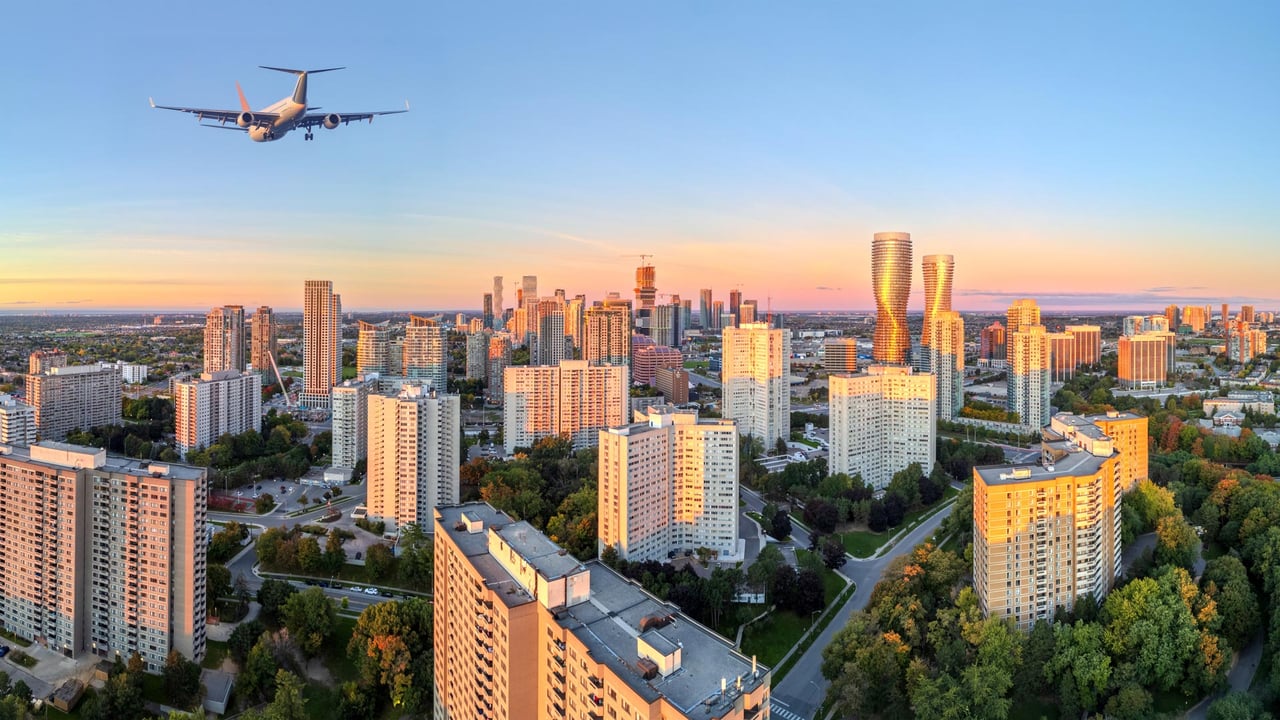 A stunning aerial golden hour photograph of the Mississauga skyline with a commercial airplane flying overhead, highlighting the city’s connectivity and urban appeal for those moving to Mississauga