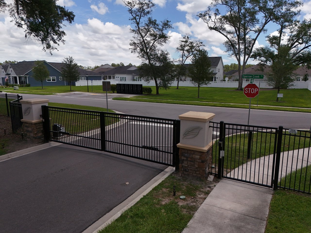 Residential community entrance with a black metal gate, homes, and a Sparrow Creek Dr street sign.
