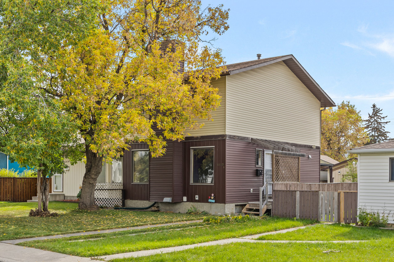 Two-story beige and brown house beside a large yellow-leaved autumn tree.