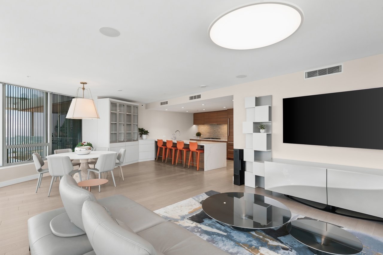 Open-plan living room with a white sectional, round dining table, and kitchen island with orange bar stools.