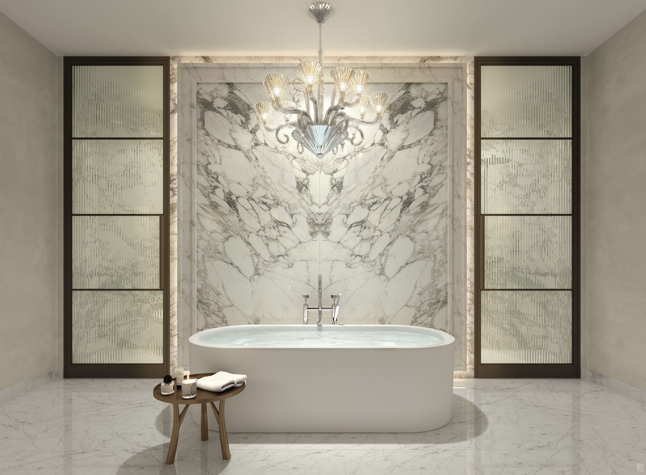 Luxury bathroom with a freestanding tub, book-matched marble wall, and crystal chandelier.