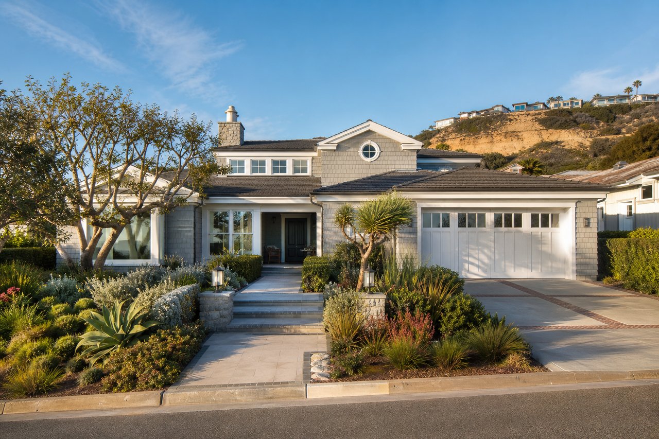 Shingle-sided home with a landscaped entry, attached garage, and homes on a bluff behind it.
