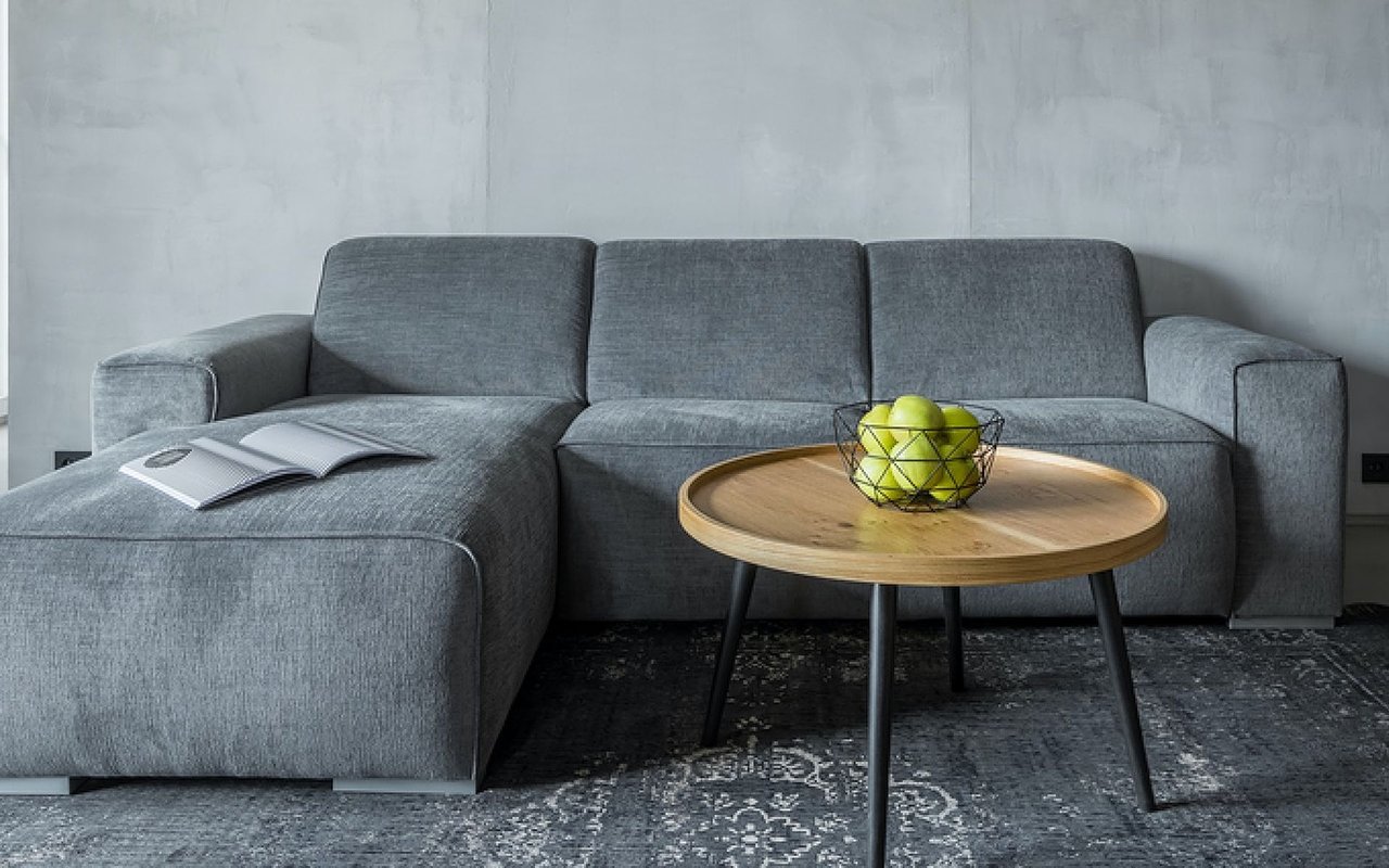 Gray sectional sofa and round wood coffee table with green apples in a modern living room.