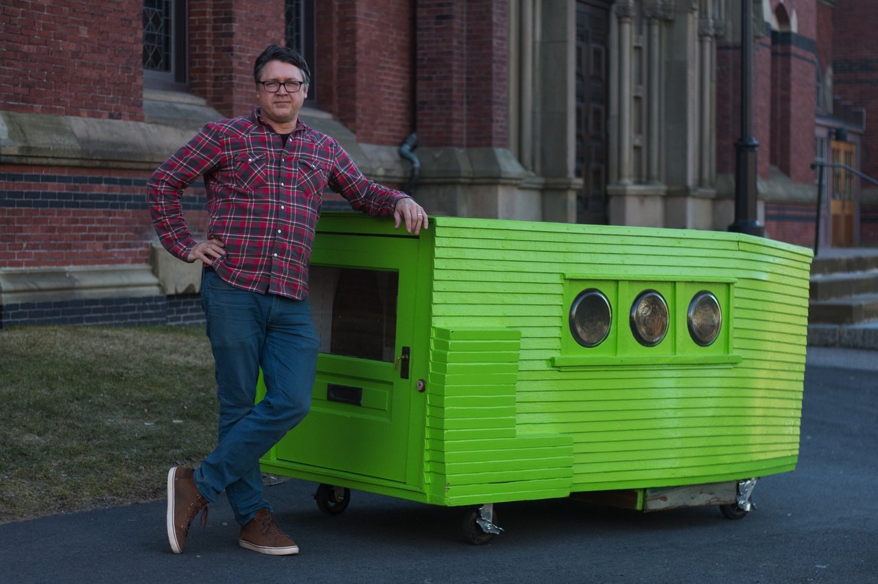 Bright green tiny house on wheels with three round windows, beside a man.