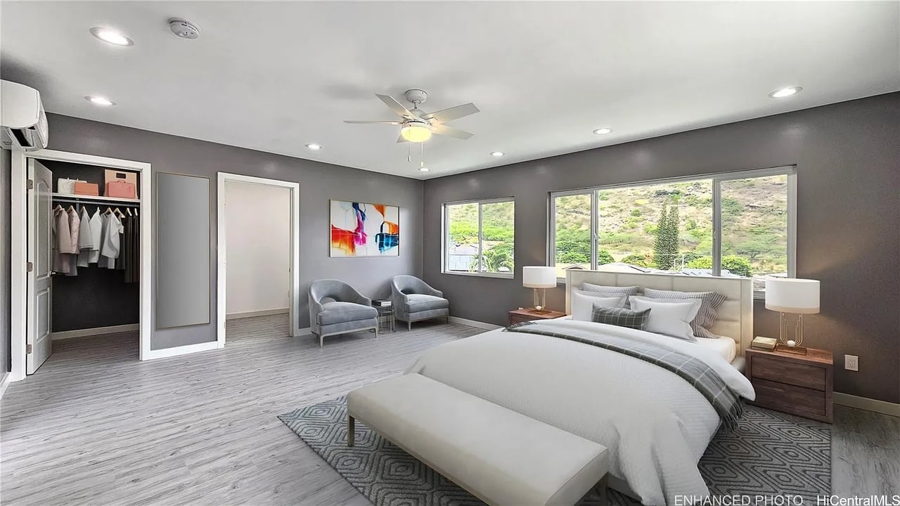 Furnished bedroom with a white bed, sitting area, open closet, and hillside views.