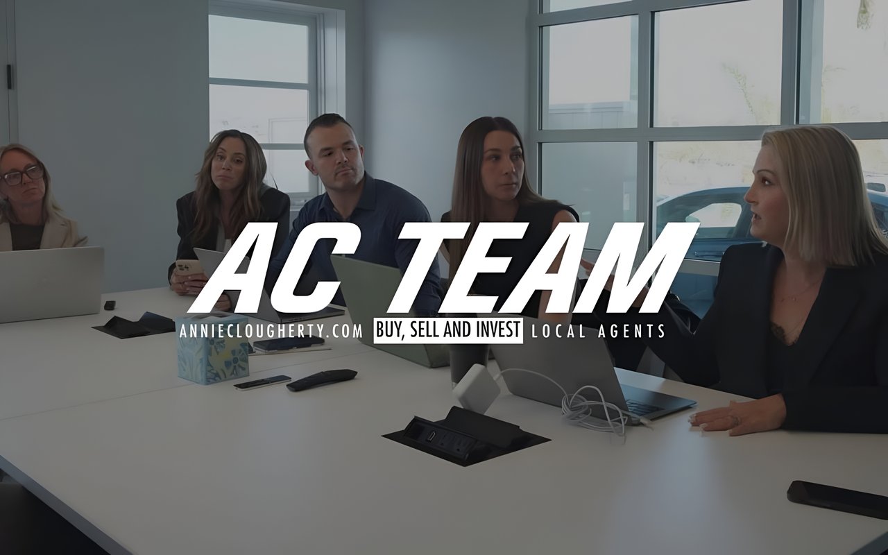  A business team of five people sits around a conference table with laptops and phones, engaged in a discussion.