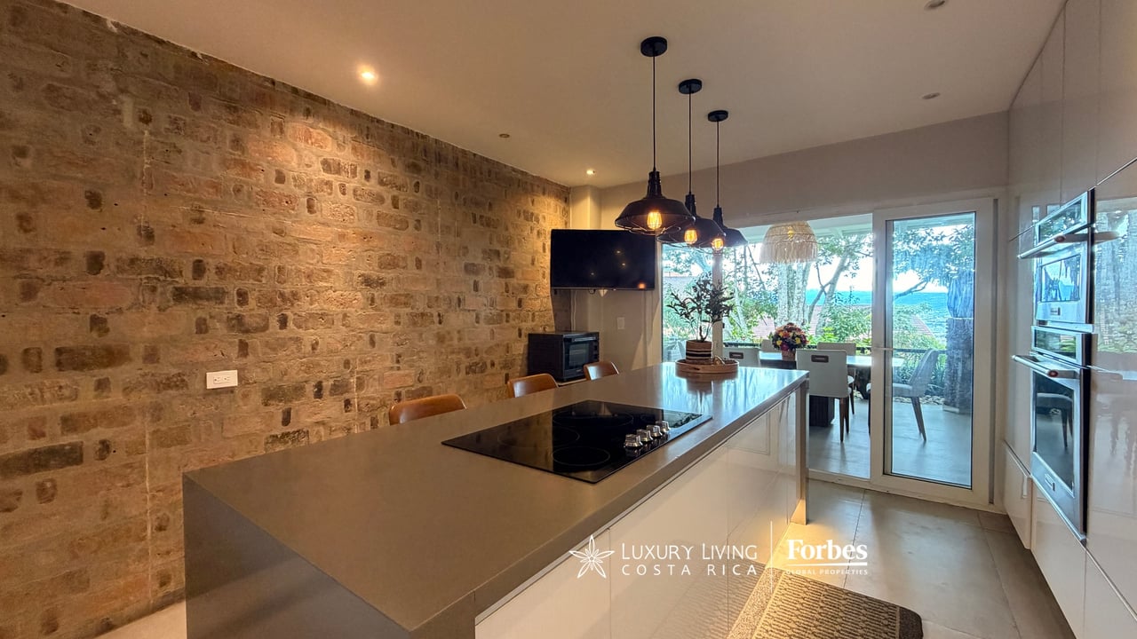 Kitchen with a stone island and cooktop, exposed stone wall, and sliding doors to a leafy patio.