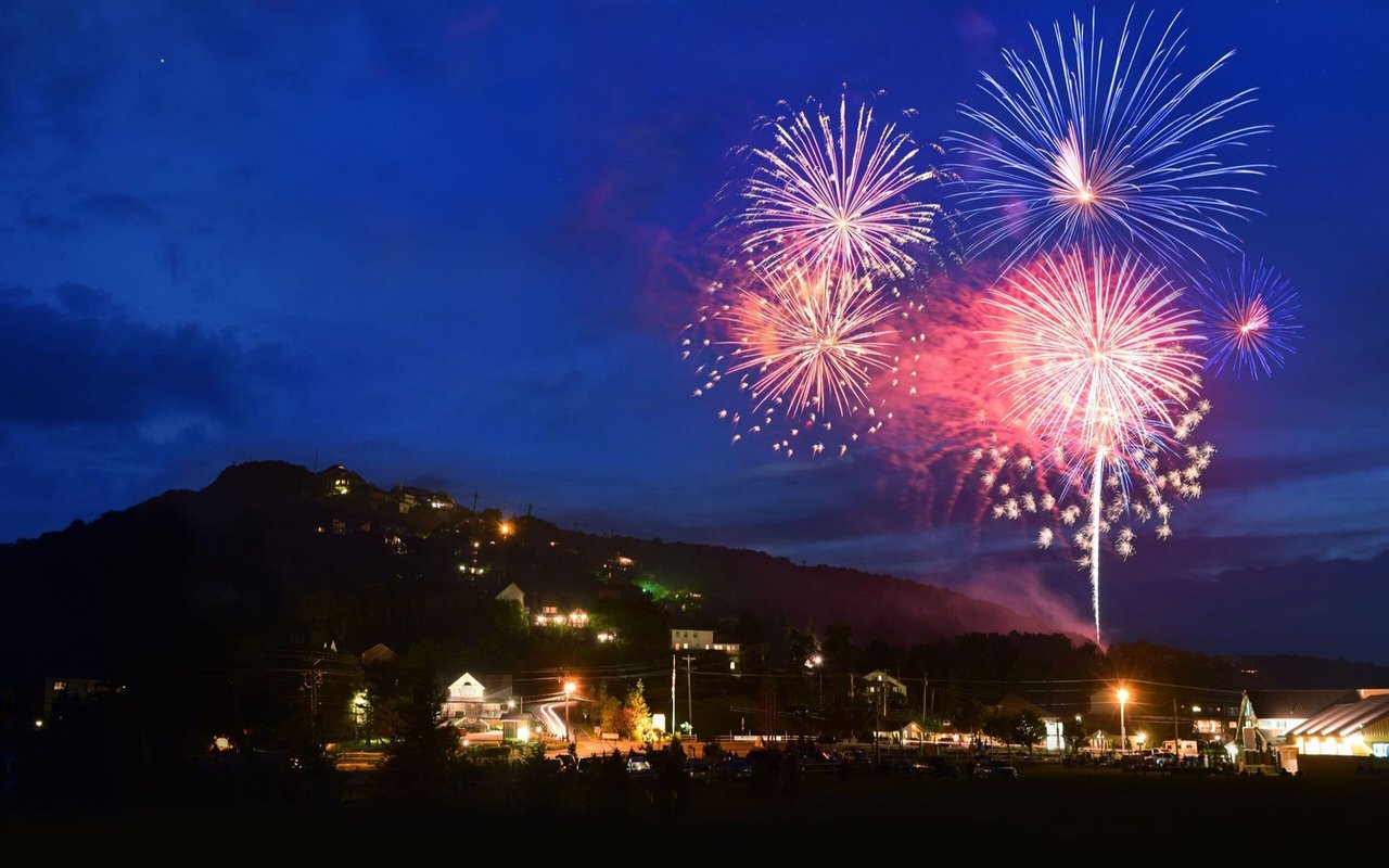 Colorful Fourth of July fireworks burst above a hillside town at night.