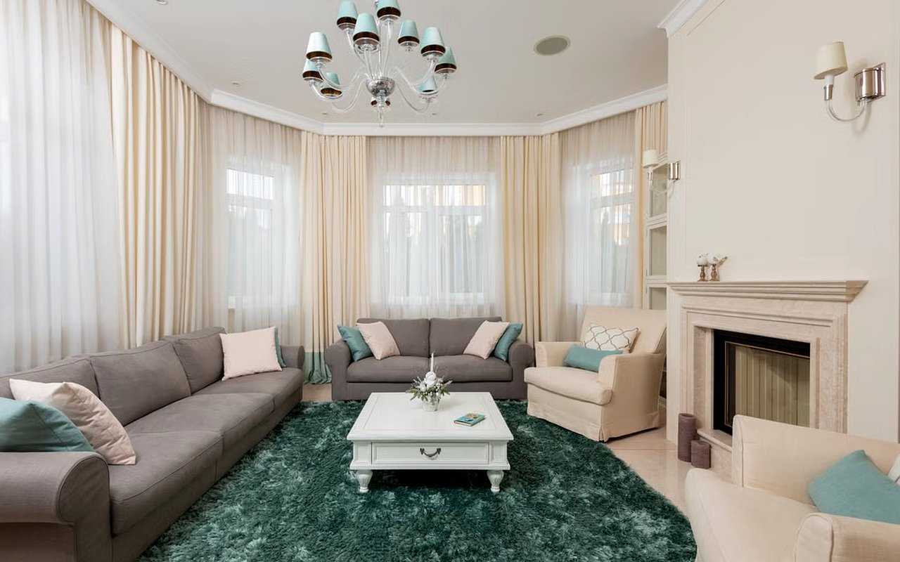 Living room with gray sofas, a deep green rug, tall curtained windows, and a fireplace.