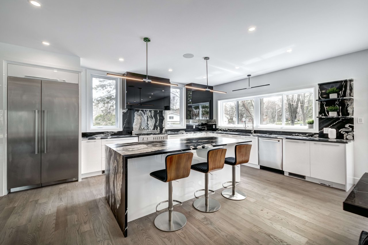 Modern kitchen with a dramatic veined marble island and three wooden bar stools.