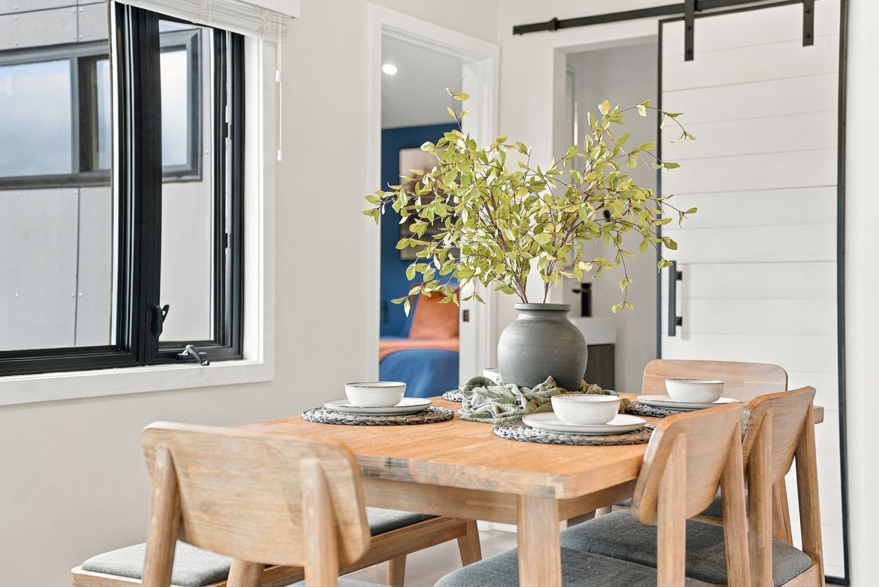 Dining room with a set wooden table, leafy centerpiece, black-framed window, and white sliding barn door.