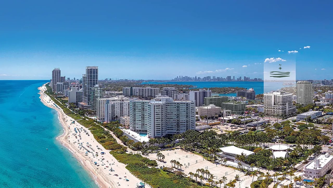 Aerial view of beachfront high-rises, sandy shoreline, and turquoise water along a coastal city.