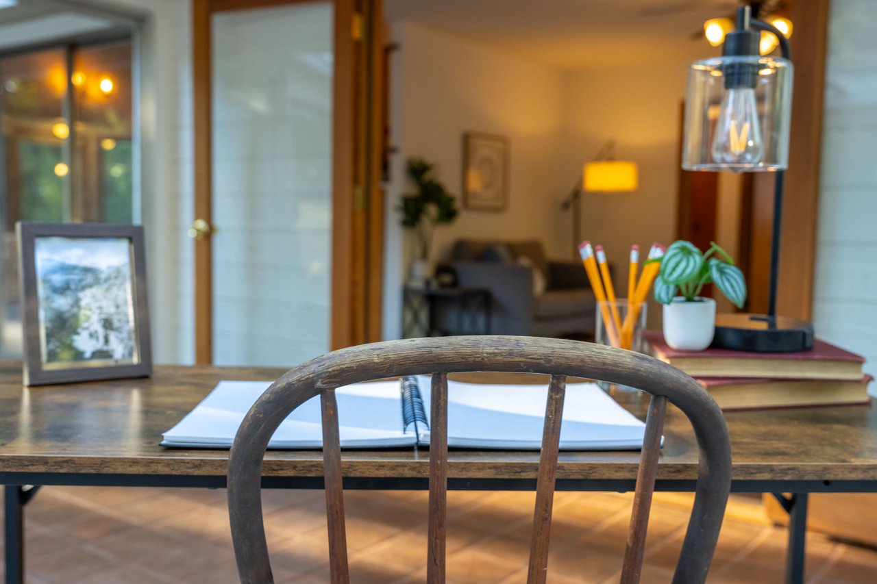 Desk with an open notebook and pencils, overlooking a warmly lit living area.