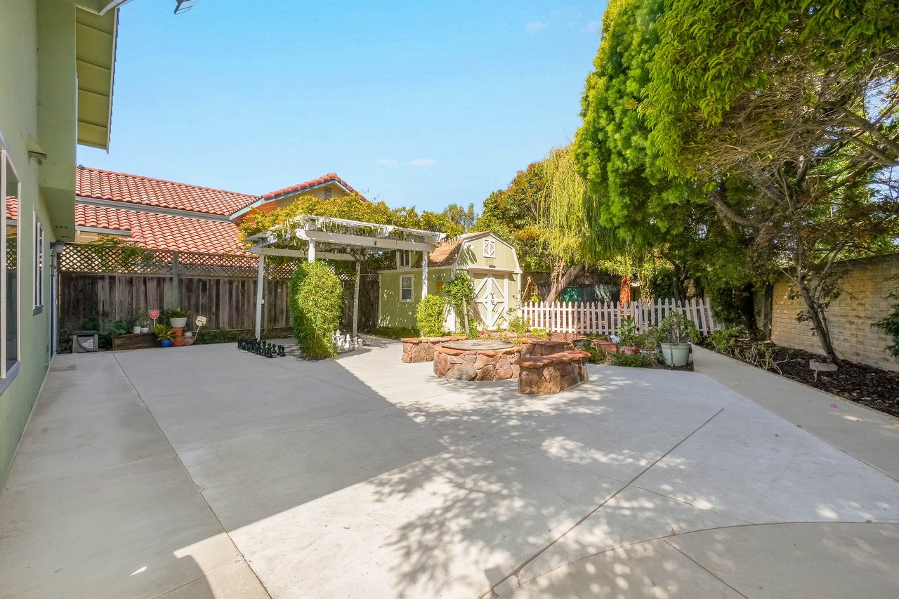 Backyard patio with a stone fire pit, pergola, garden shed, and white picket fence.