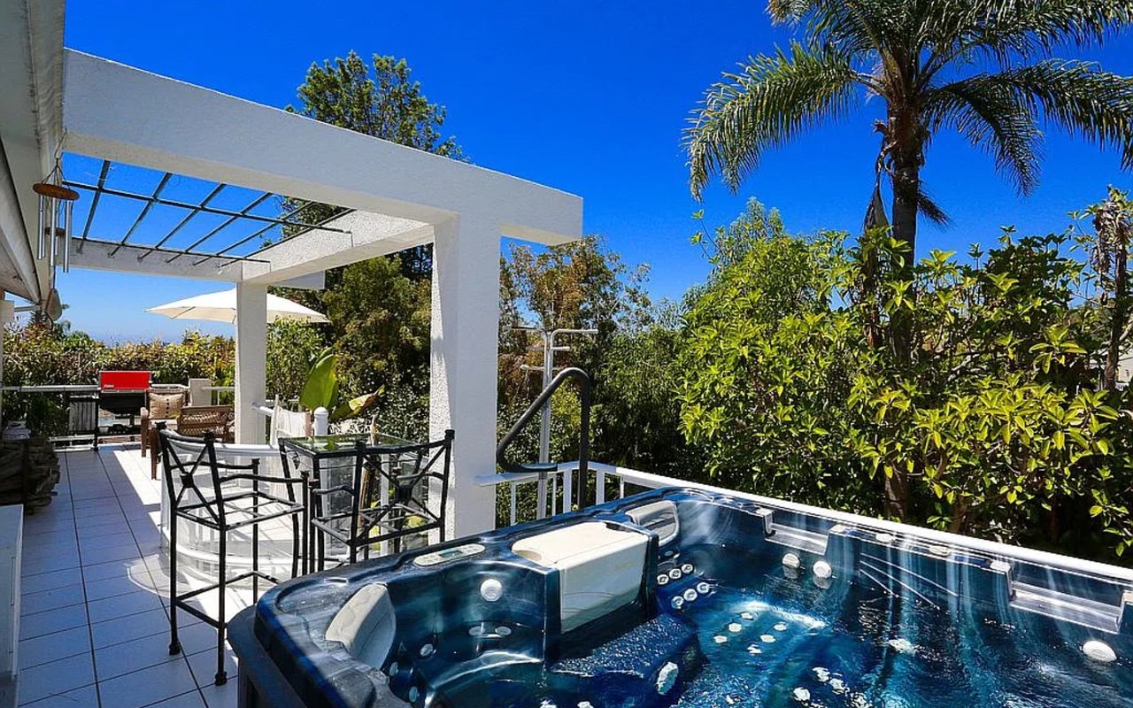 Outdoor patio with a large hot tub, white pergola, and glass-top dining table.