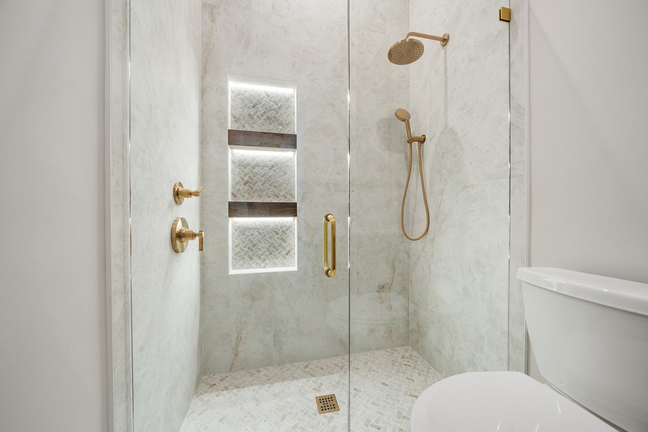 Walk-in shower with pale tile, illuminated niches, and brushed-gold fixtures.