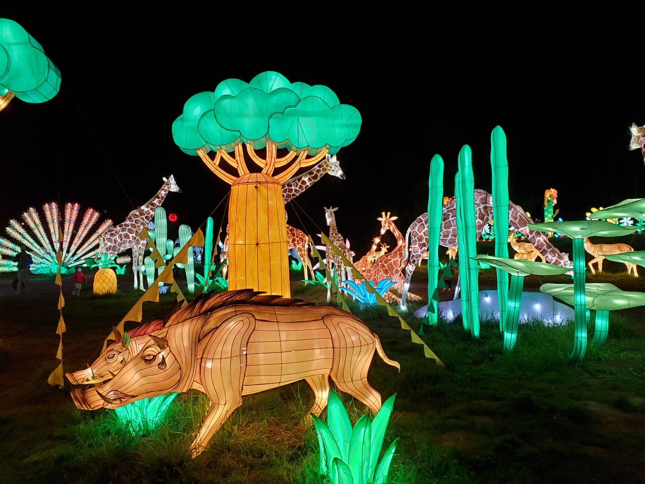 Illuminated animal lanterns, including giraffes and a warthog, fill a nighttime garden display.