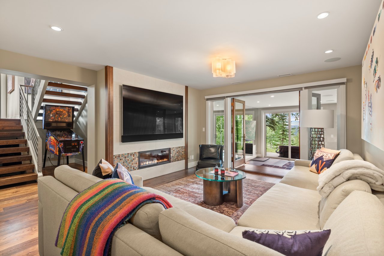 Living room with cream sofas, a fireplace, wall-mounted television, pinball machine, and sliding glass doors.