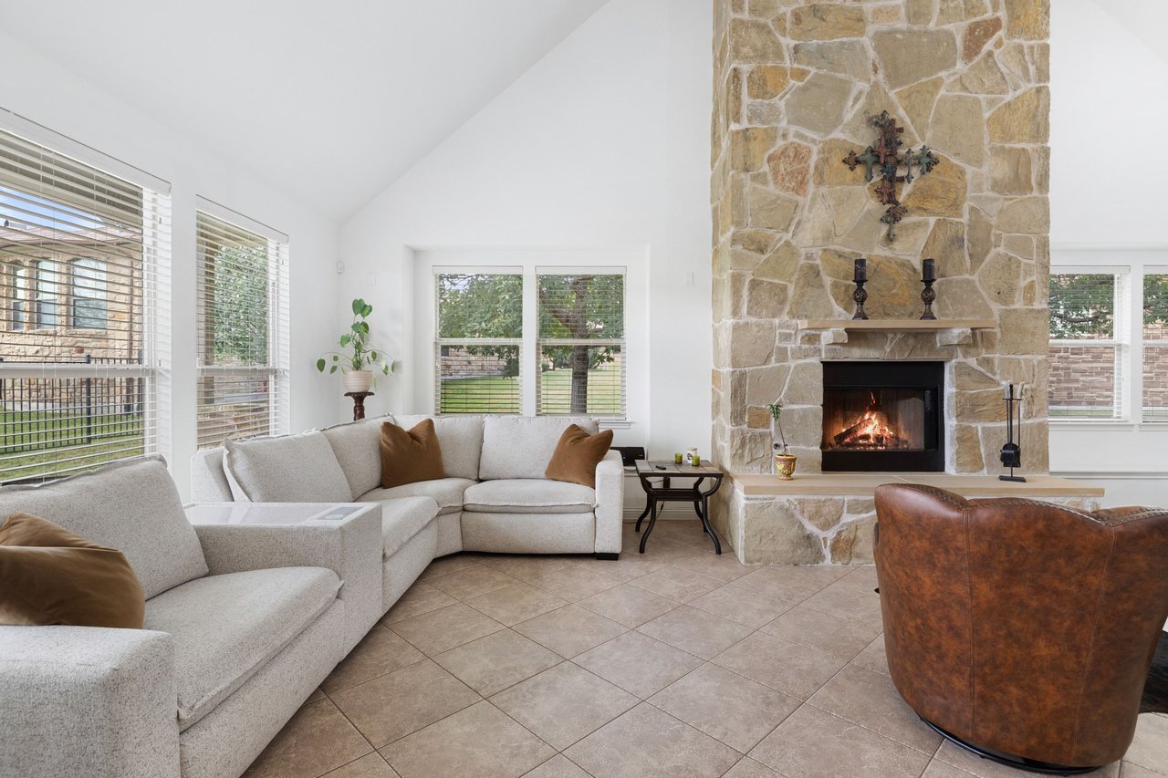 Living room with a tall stone fireplace, lit fire, vaulted ceiling, and pale sectional sofas.