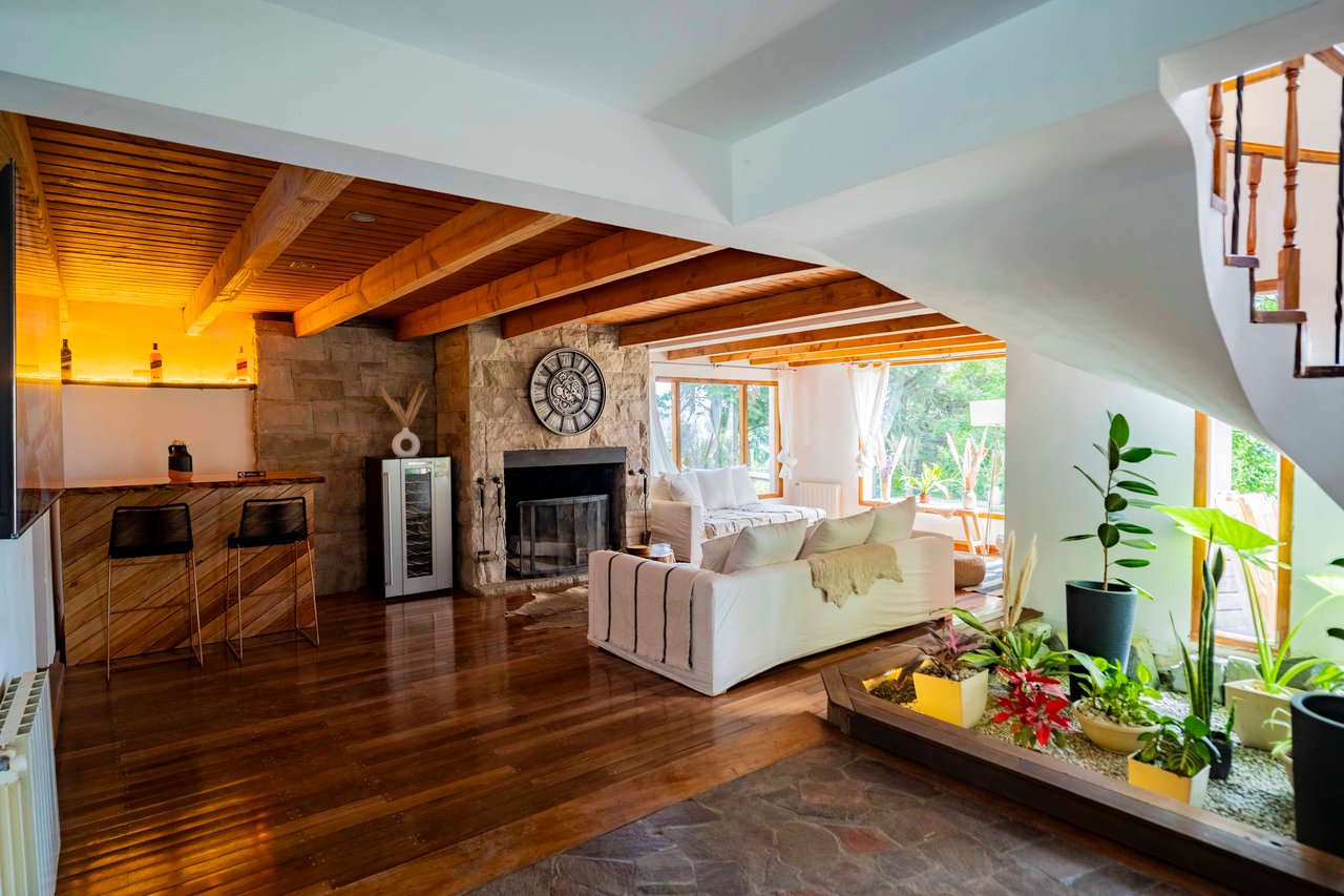 Boutique hotel living room with a stone fireplace, exposed wood beams, and a raised planter of tropical plants.
