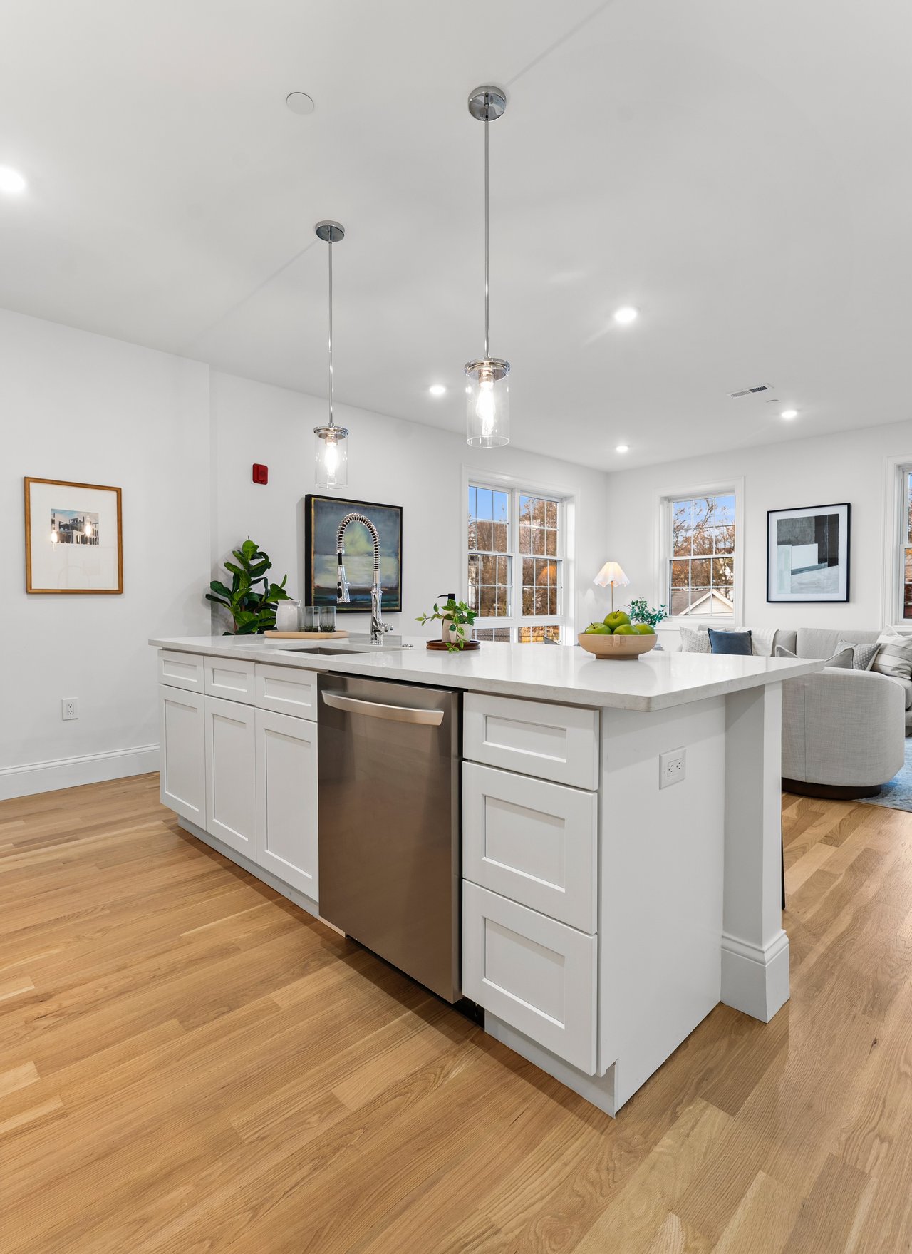 Bright kitchen with a large white island, stainless dishwasher, pendant lights, and hardwood floors.