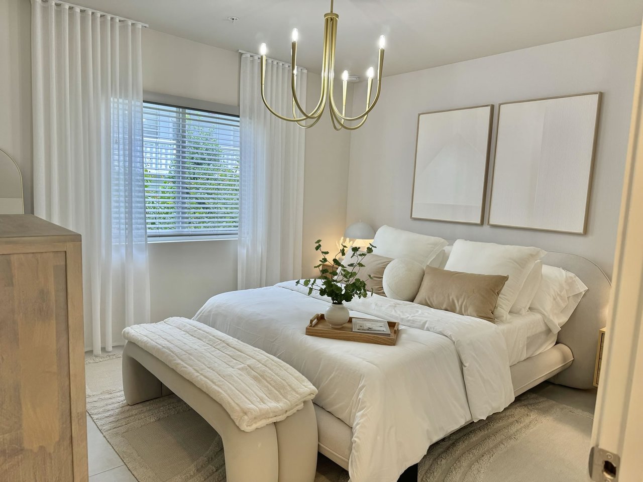 Staged bedroom with a white upholstered bed, sheer curtains, and a brass chandelier.