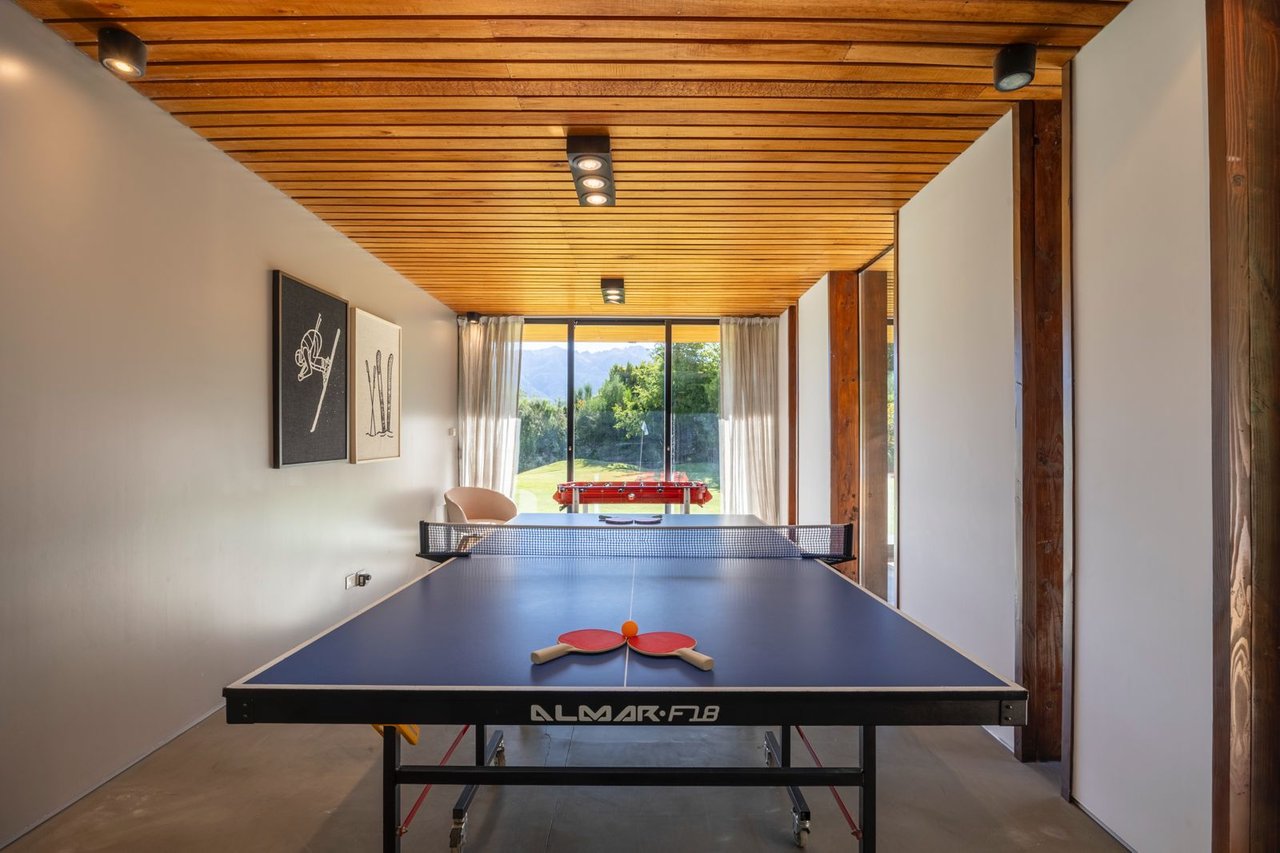 Game room with a blue ping-pong table, wood-slat ceiling, and garden views.