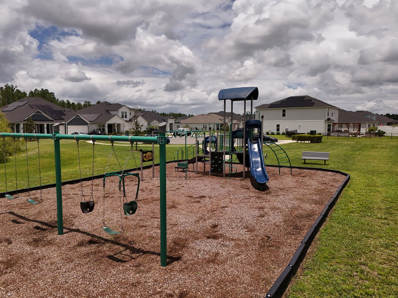 Neighborhood playground with swings and a blue slide, with suburban homes in the background.