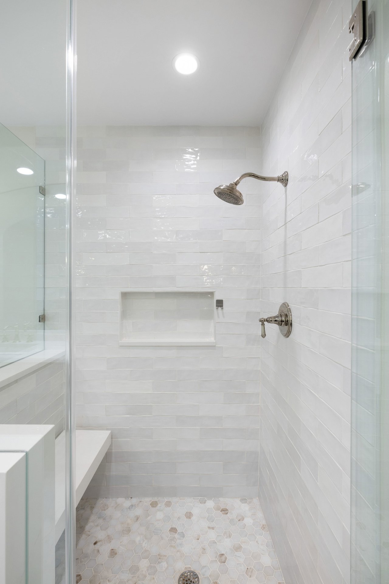 Walk-in shower with glossy white tile, a built-in niche, chrome fixtures, and a hexagonal tile floor.