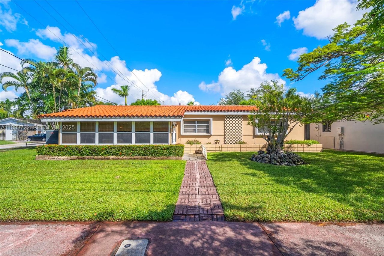 Single-story beige home with a terracotta tile roof, screened porch, and tropical landscaping.