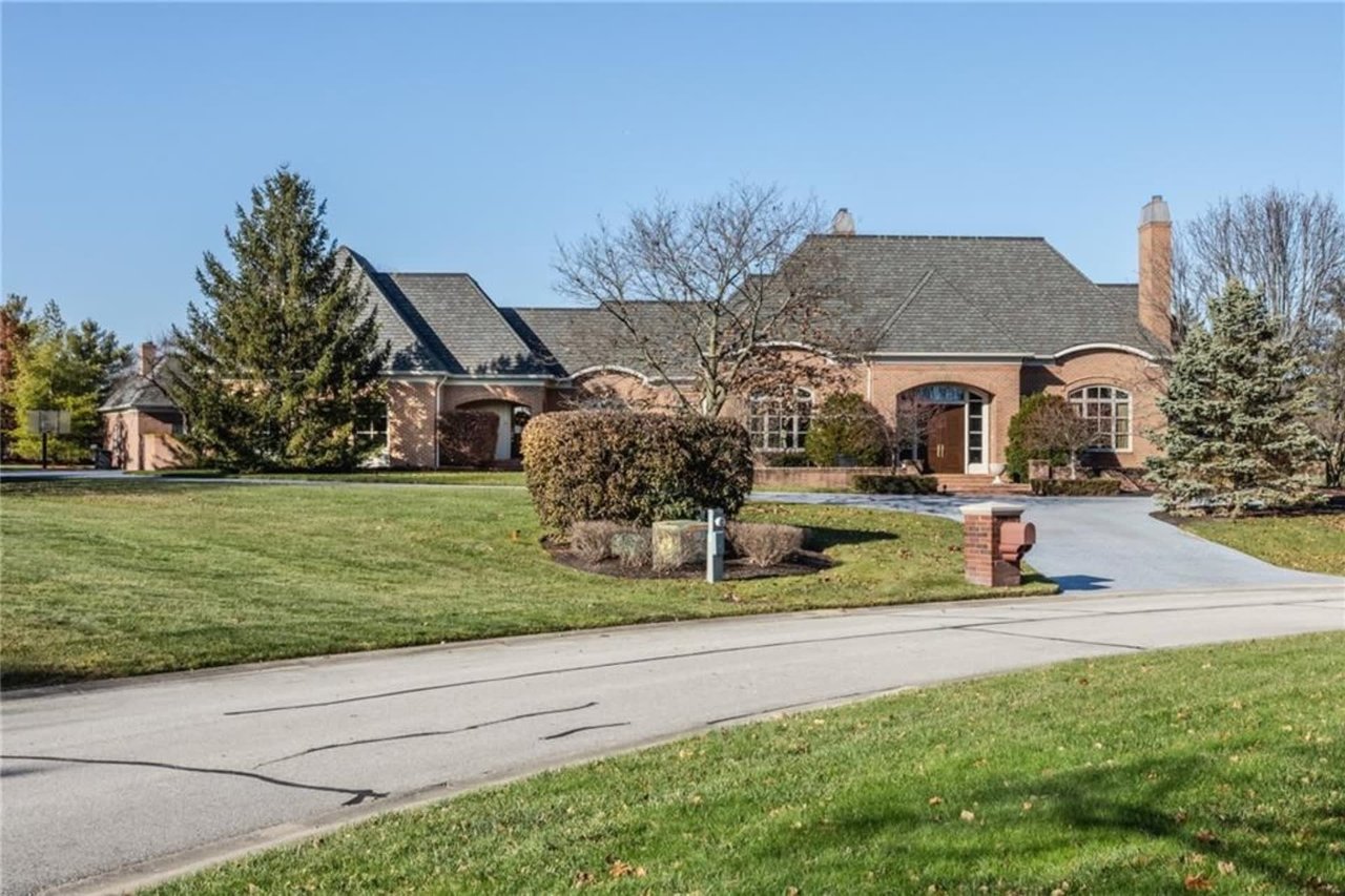 Luxury brick ranch estate showcasing a multi-gabled roofline, arched windows, formal entryway, professional landscaping, and an expansive yard under a clear blue sky.