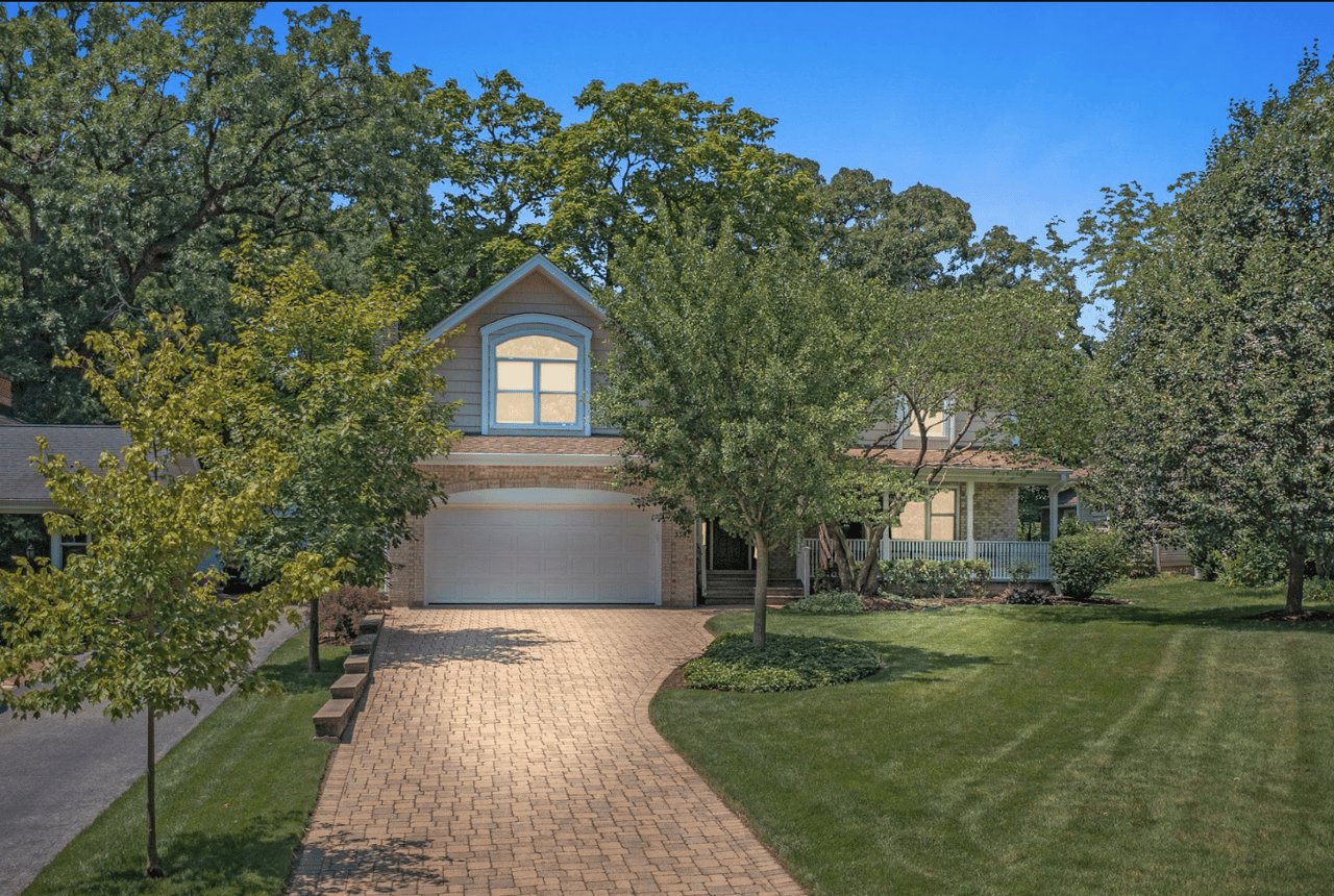 Two-story home in Downers Grove, Illinois, featuring mature trees, a landscaped front lawn, and a brick paver driveway.
