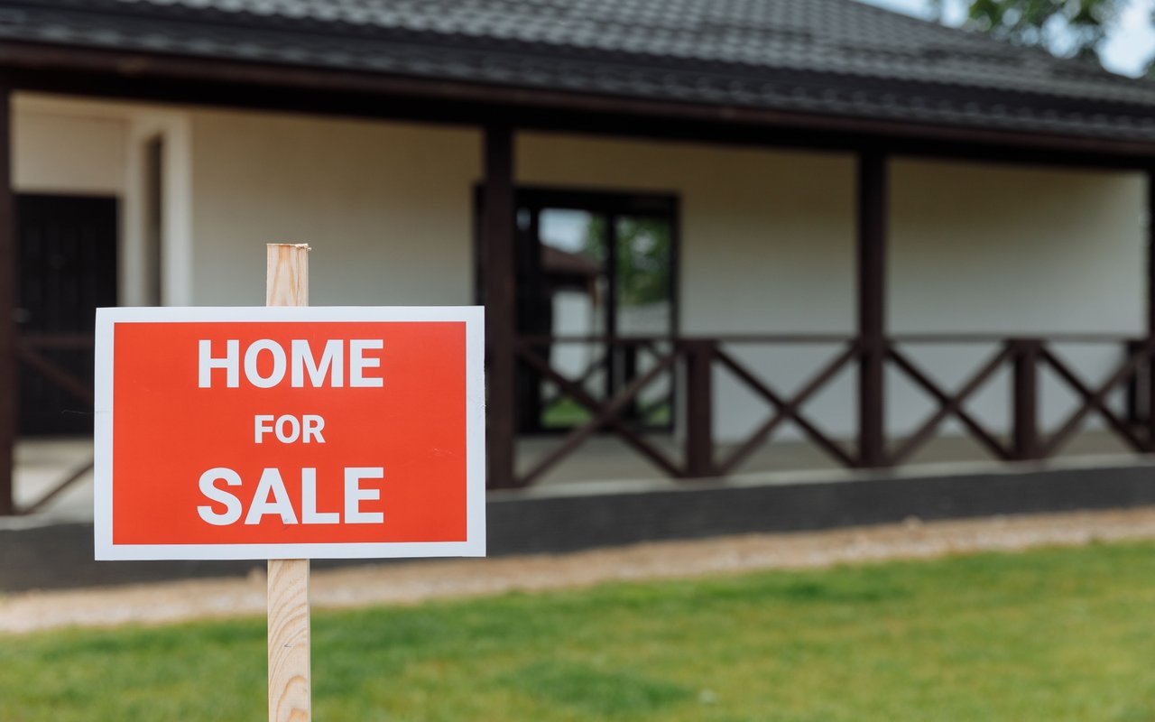 House for sale with a red sign in front of its covered porch.