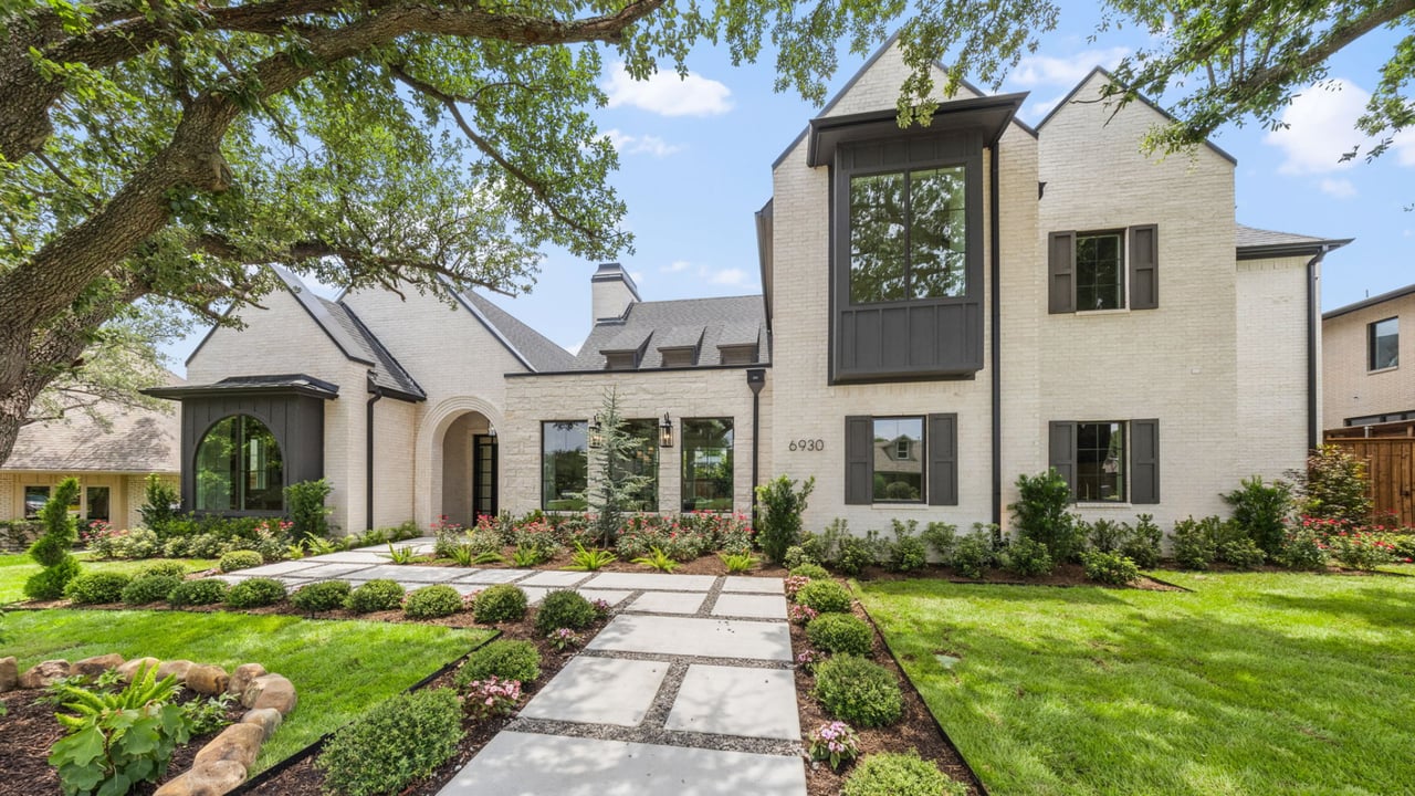 White brick two-story home with dark trim, landscaped walkway, and a mature tree in the foreground.