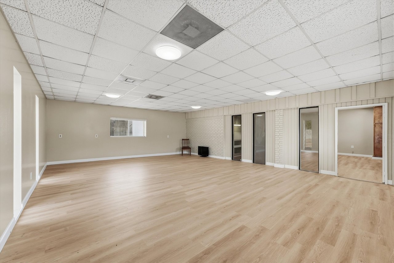 Large mostly empty room with light wood floors, a white brick wall, and several doorways.