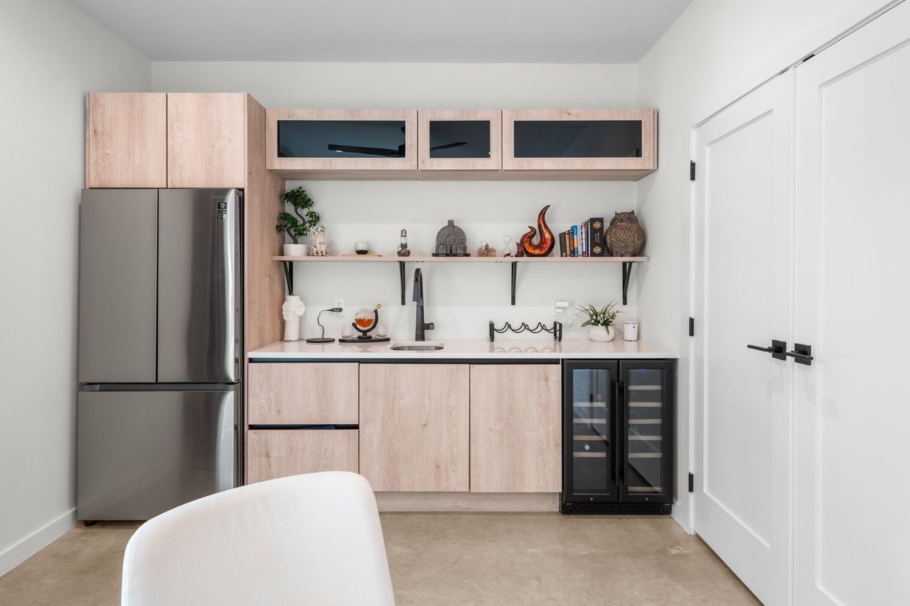 Wet bar with light wood cabinets, stainless steel refrigerator, sink, and under-counter wine coolers.