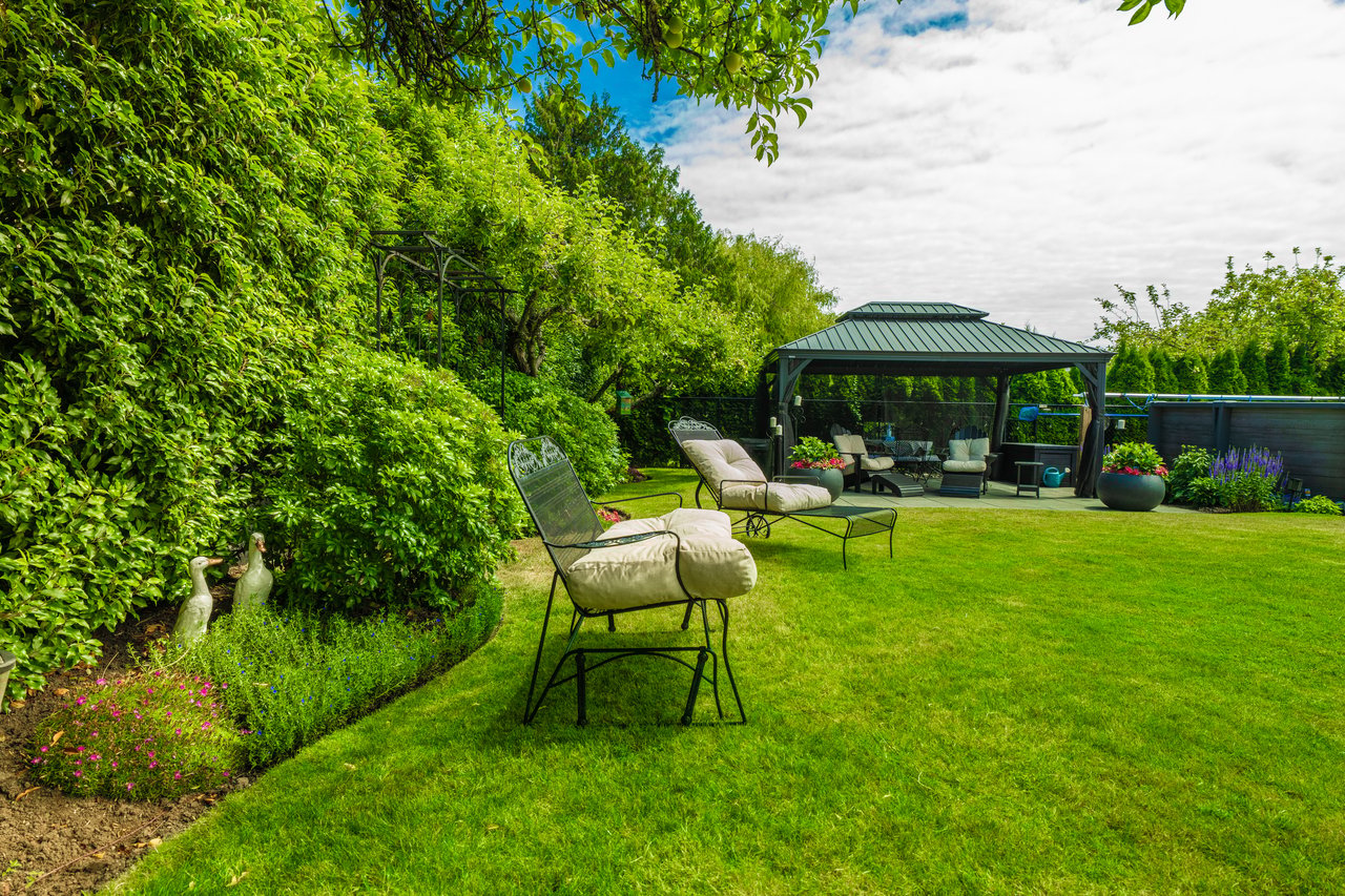 Landscaped backyard with a lawn, cushioned lounge chairs, and a covered gazebo.