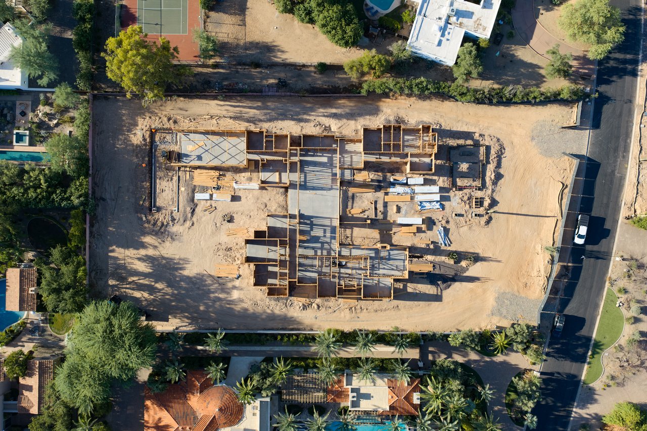 Aerial view of a home under construction, showing its foundation and framing amid neighboring properties.