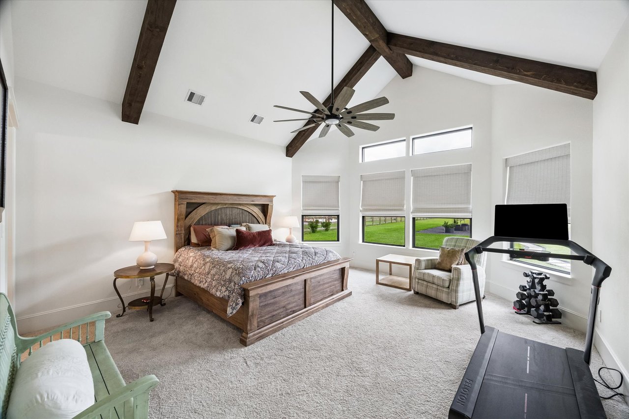 Bedroom with vaulted exposed-beam ceiling, large windows, king bed, and exercise equipment.