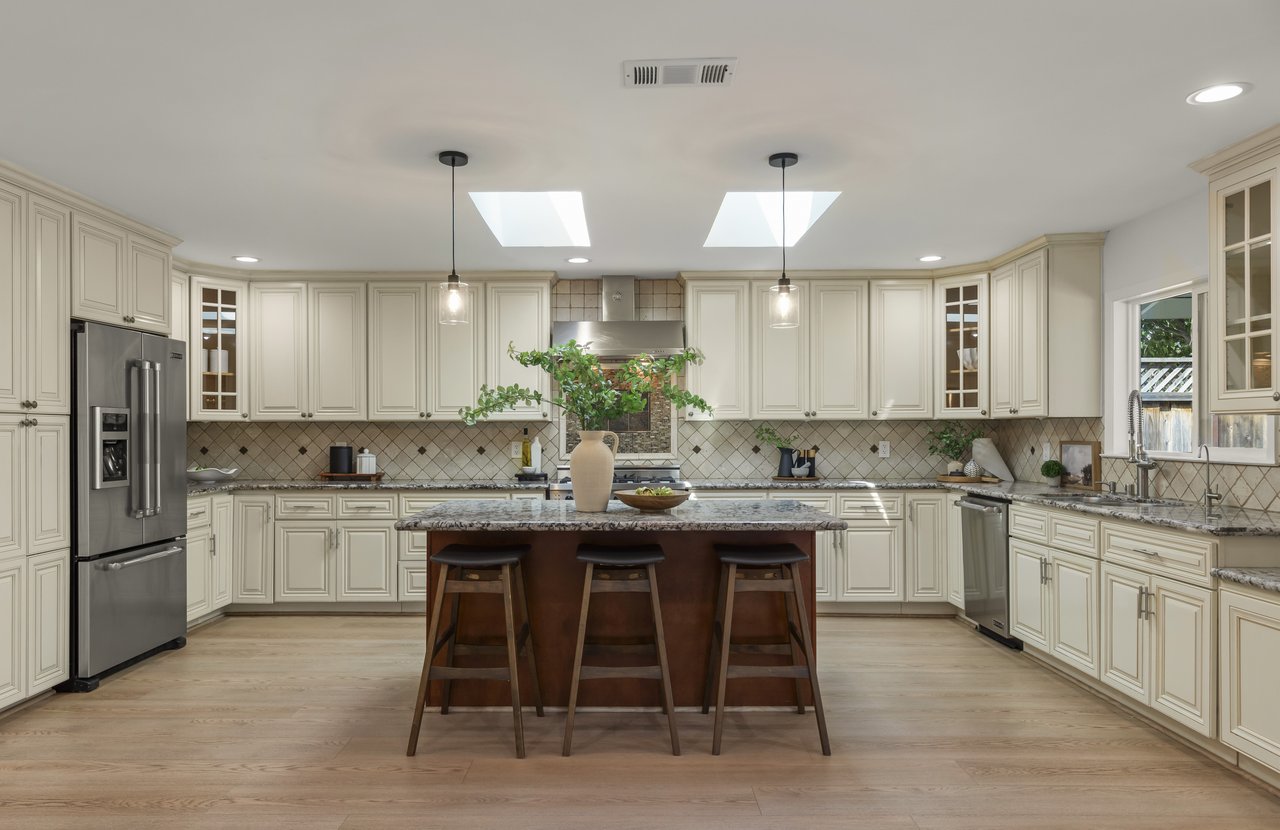 Spacious cream kitchen with a large island, three stools, patterned tile backsplash, and two skylights.