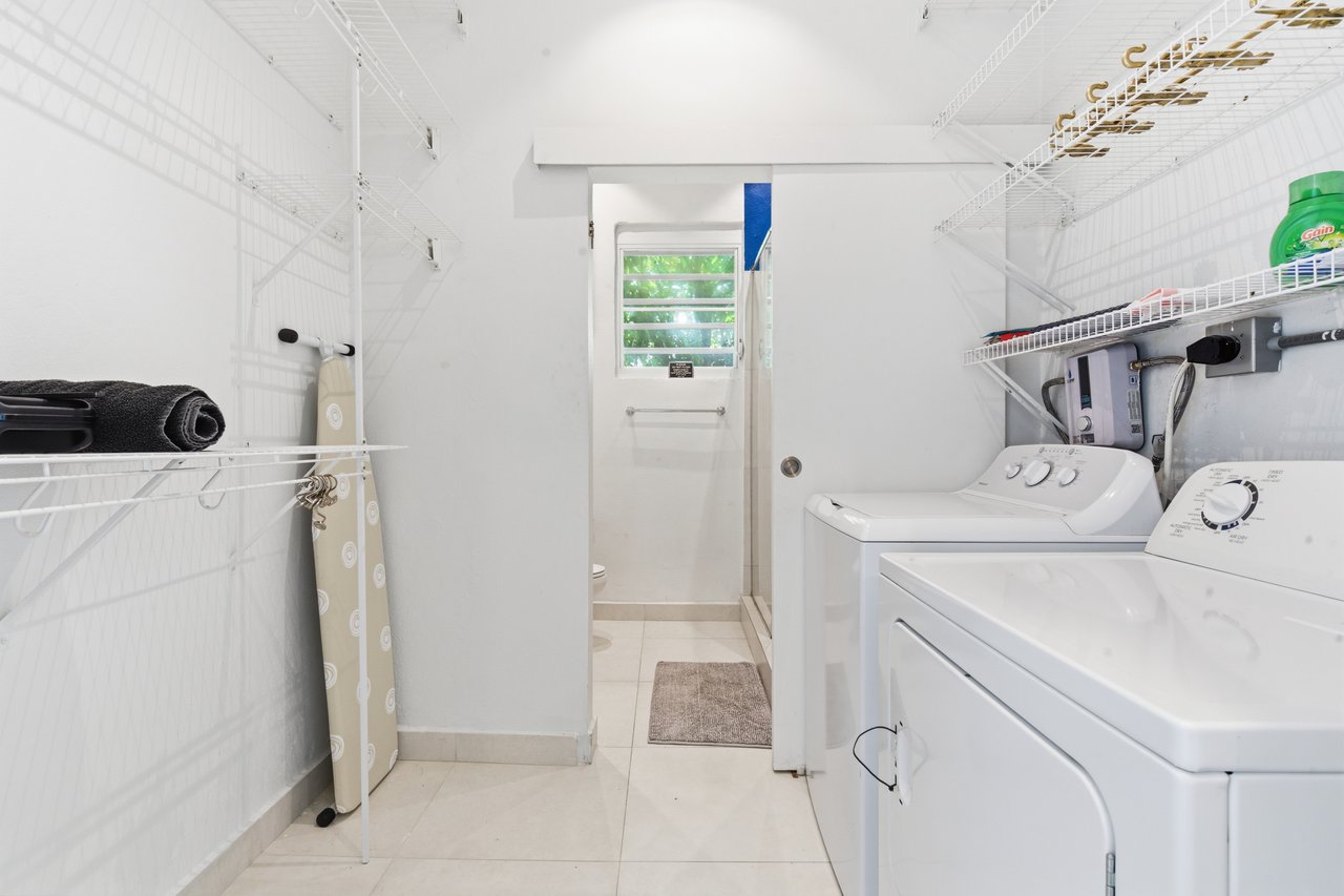Laundry room with a washer and dryer, white wire shelving, and an ironing board.