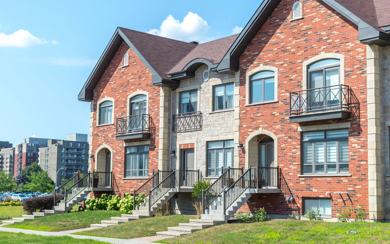 Brick and stone townhomes with metal balconies, front stairs, and a landscaped lawn.