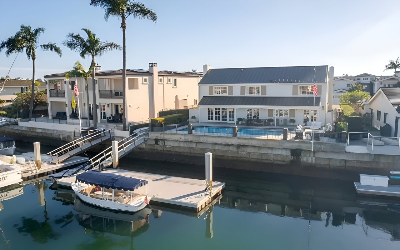  A luxurious waterfront home with a pool, a dock with a small boat, and a view of the bay.
