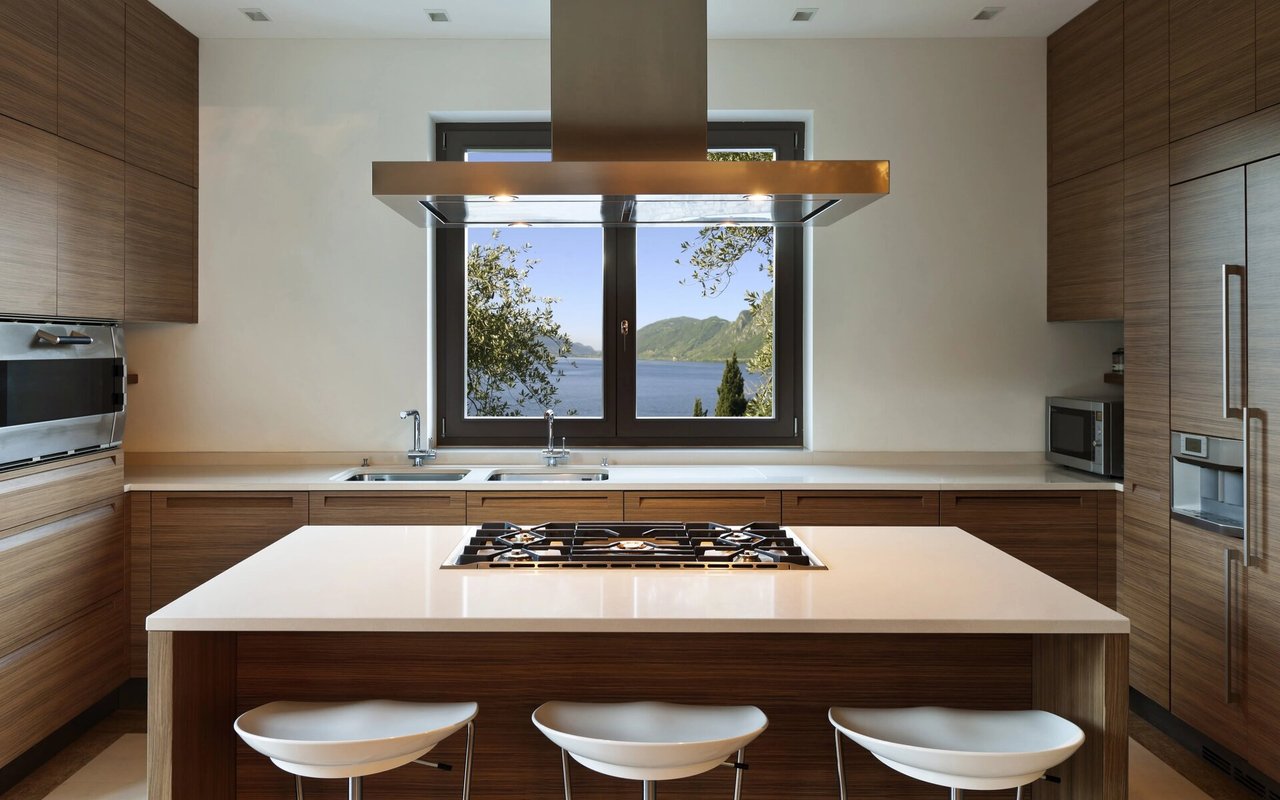 Modern kitchen with a white cooktop island and a window overlooking water and mountains.