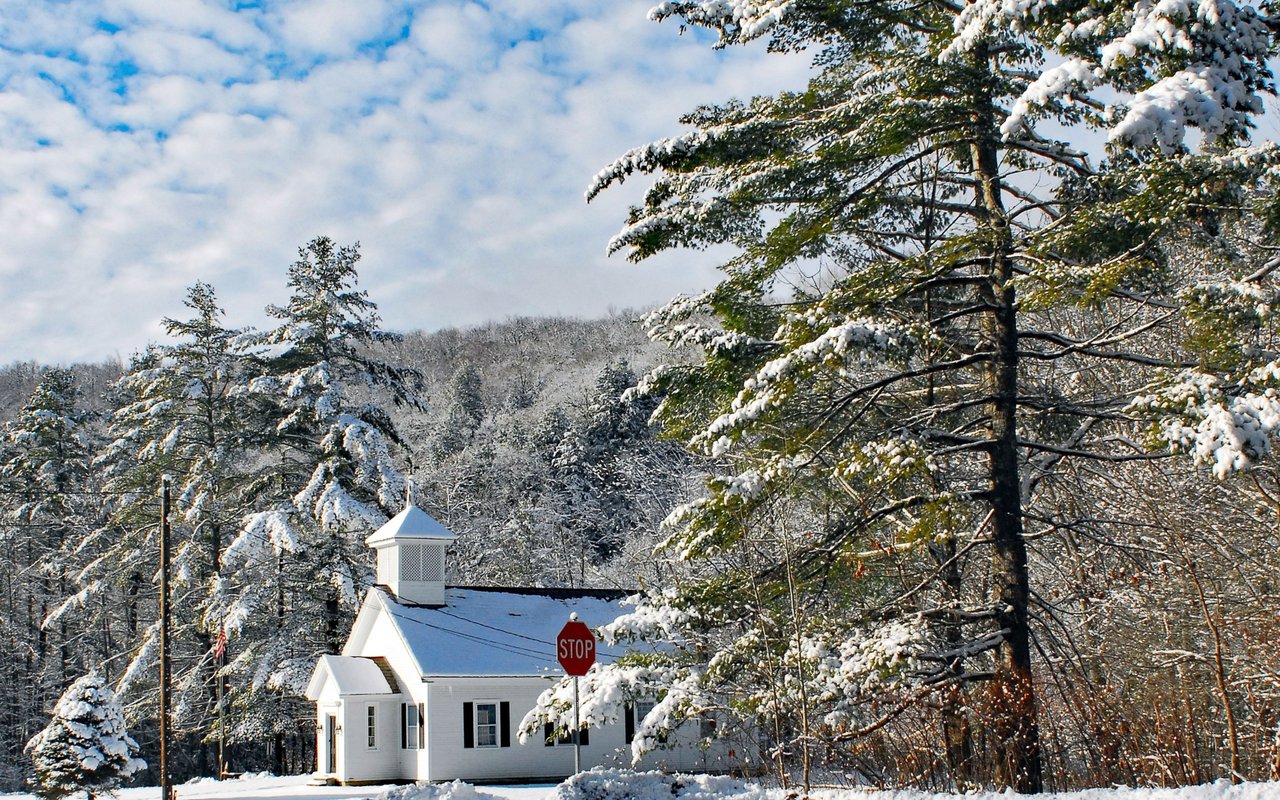 A small white church stands among snow-covered trees beside a stop sign.