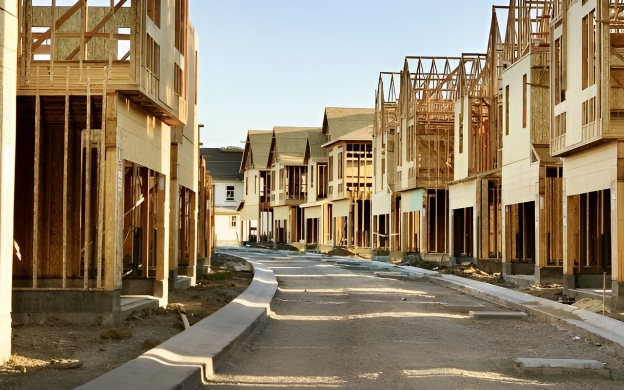 New homes under construction line an unfinished residential street, with exposed wood framing and incomplete sidewalks.