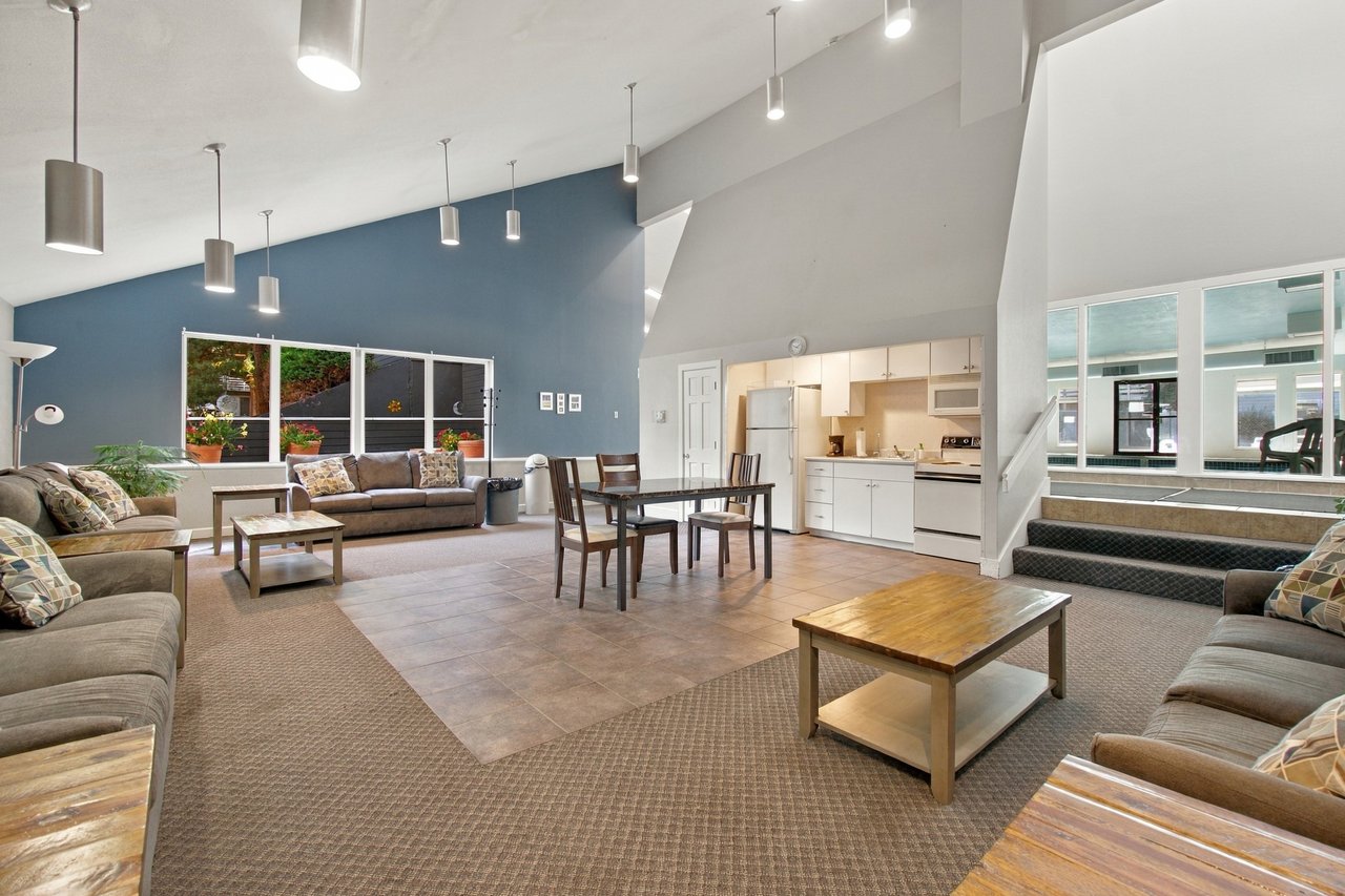 Furnished lounge and dining area with a compact kitchen and indoor pool visible through the windows.