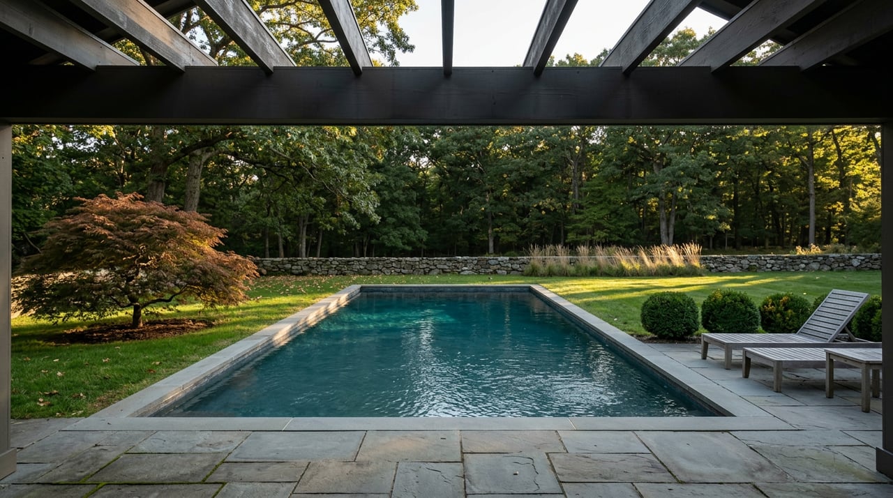 Rectangular blue-green pool beyond a bluestone patio, with a red-bronze Japanese maple and wooded backdrop.