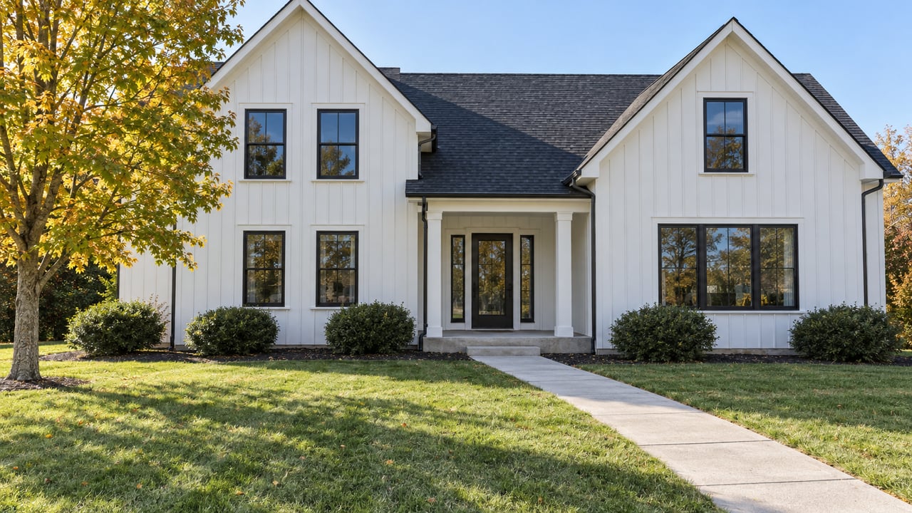 White gabled home with black-framed windows, a deep front lawn, concrete approach and a gold-green deciduous tree.
